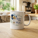 White ceramic mug on a wooden kitchen counter with blue and gold balloons and the French text 'Bonne Fête Papa'.